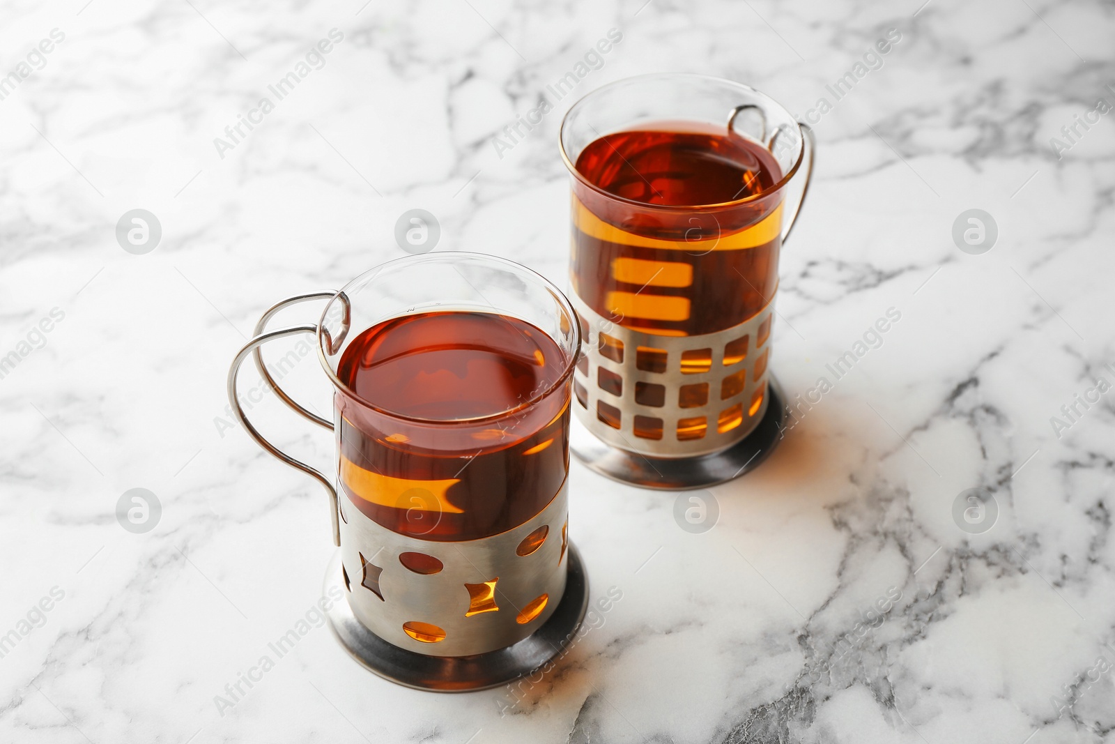 Photo of Glasses of tea in metal holders served on white marble table, closeup