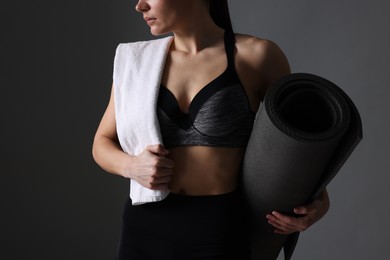 Sporty woman with terry towel and fitness mat on dark grey background, closeup