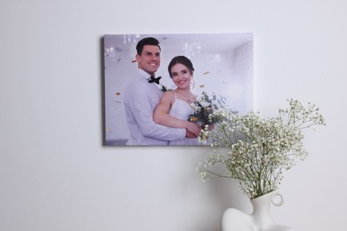 Canvas with printed photo of happy newlyweds on white wall indoors