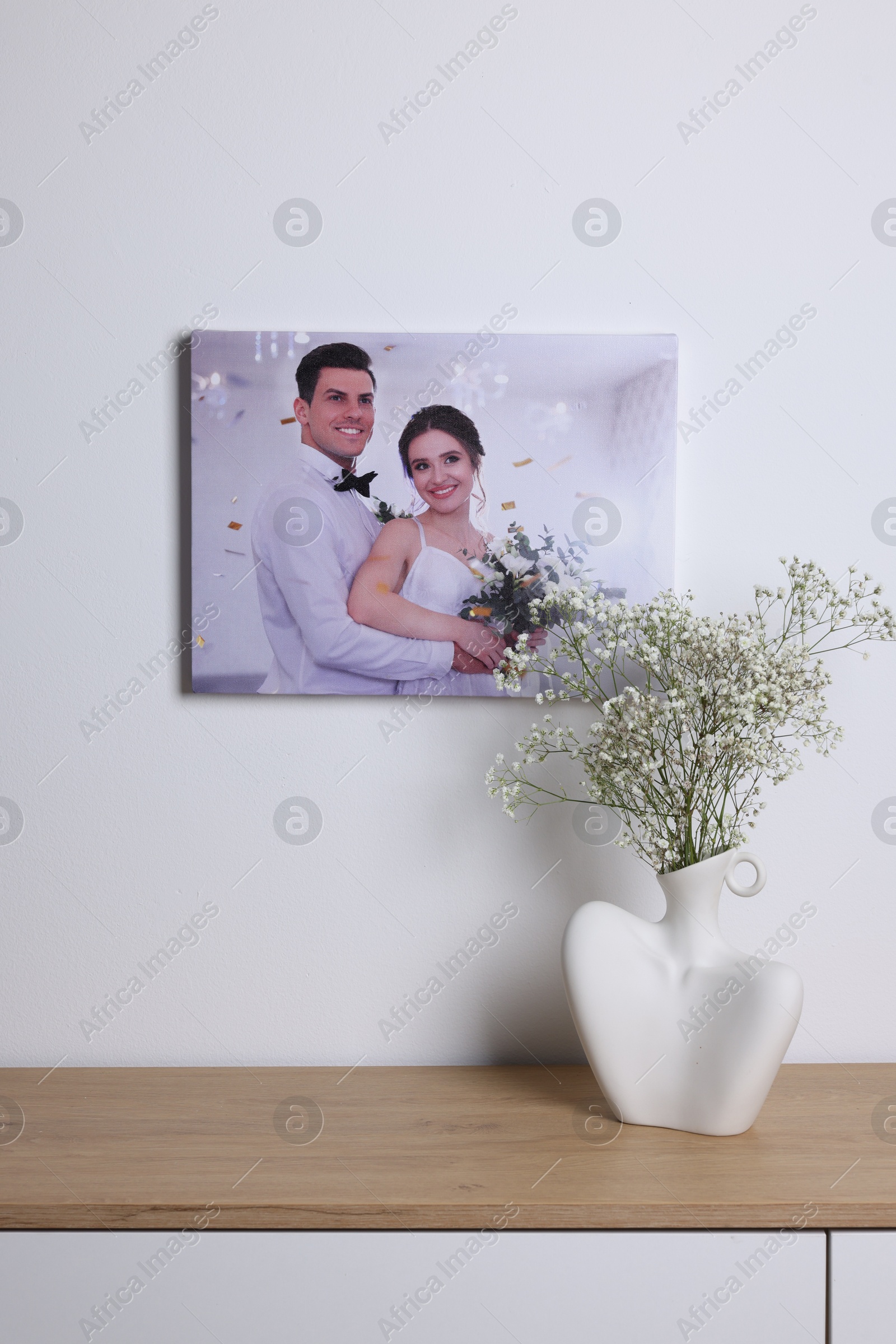 Photo of Canvas with printed photo of happy newlyweds on white wall indoors