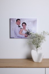 Canvas with printed photo of happy newlyweds on white wall indoors