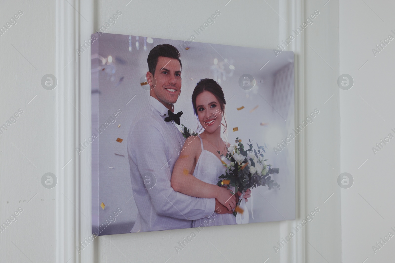 Photo of Canvas with printed photo of happy newlyweds on white wall indoors