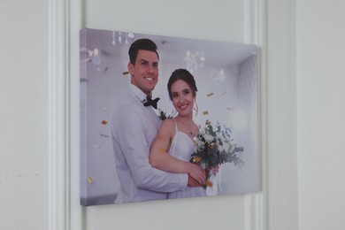 Canvas with printed photo of happy newlyweds on white wall indoors