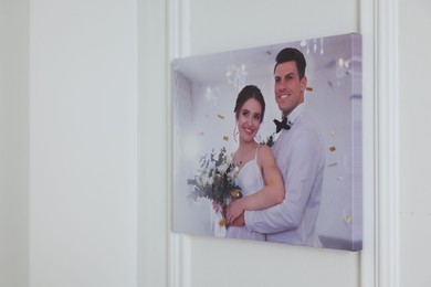 Photo of Canvas with printed photo of happy newlyweds on white wall indoors