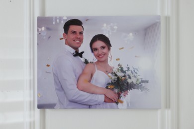 Canvas with printed photo of happy newlyweds on white wall indoors