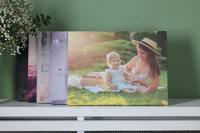 Canvas with different printed photos on shelf near green wall