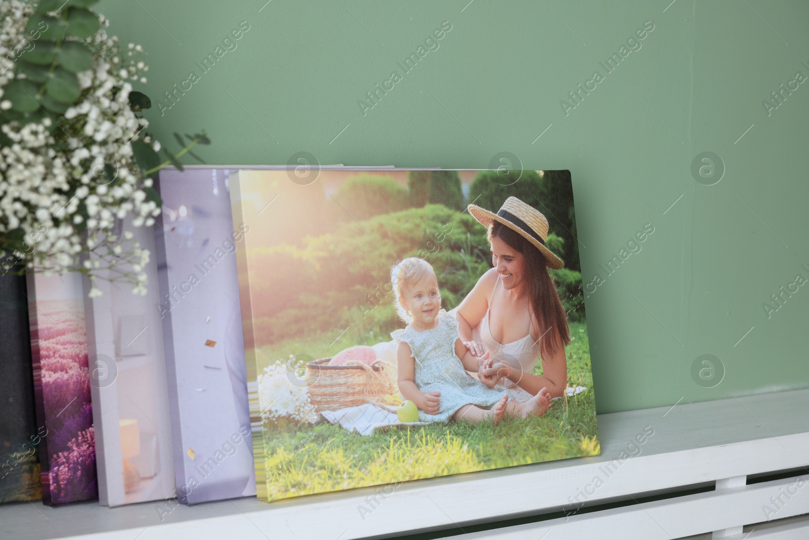 Photo of Canvas with different printed photos on shelf near green wall