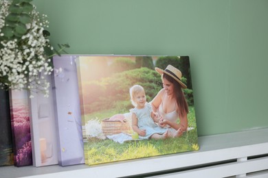 Canvas with different printed photos on shelf near green wall