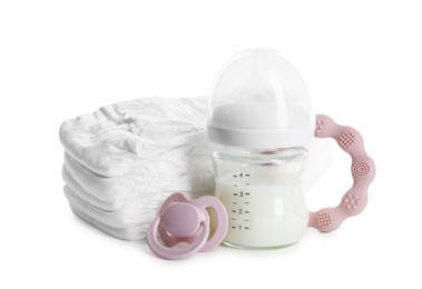 Photo of Feeding bottle with milk, diapers, teether and pacifier isolated on white