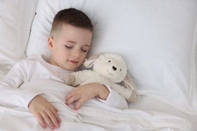 Photo of Bedtime. Cute boy sleeping with toy sheep in bed, above view