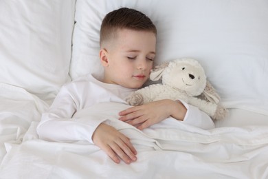 Photo of Bedtime. Cute boy sleeping with toy sheep in bed, above view