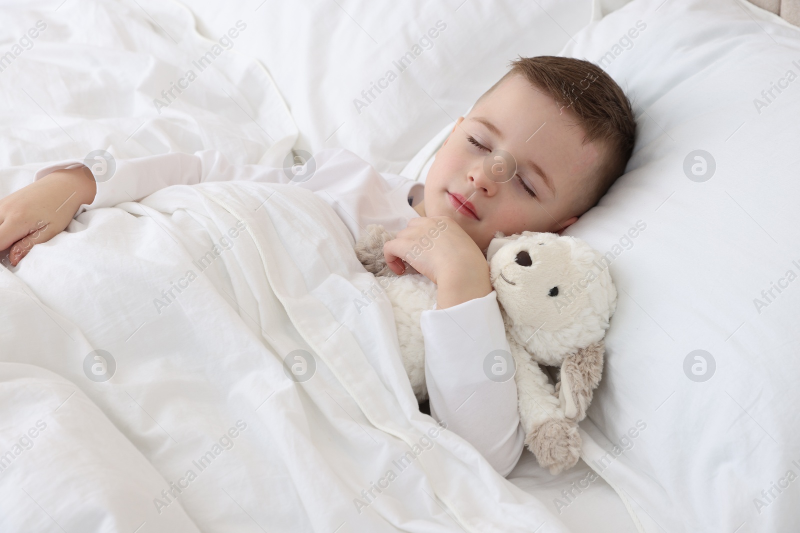 Photo of Bedtime. Cute boy sleeping with toy sheep in bed