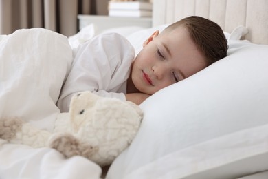 Bedtime. Cute boy sleeping with toy sheep in bed