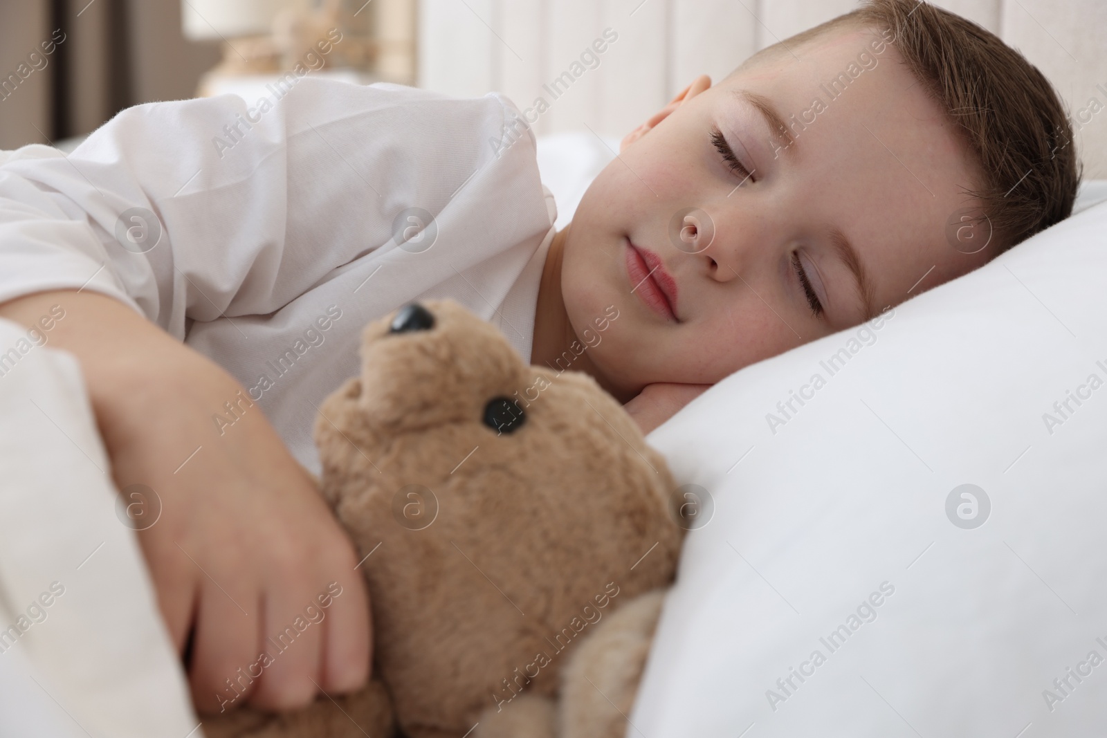 Photo of Bedtime. Cute boy sleeping with his teddy bear in bed