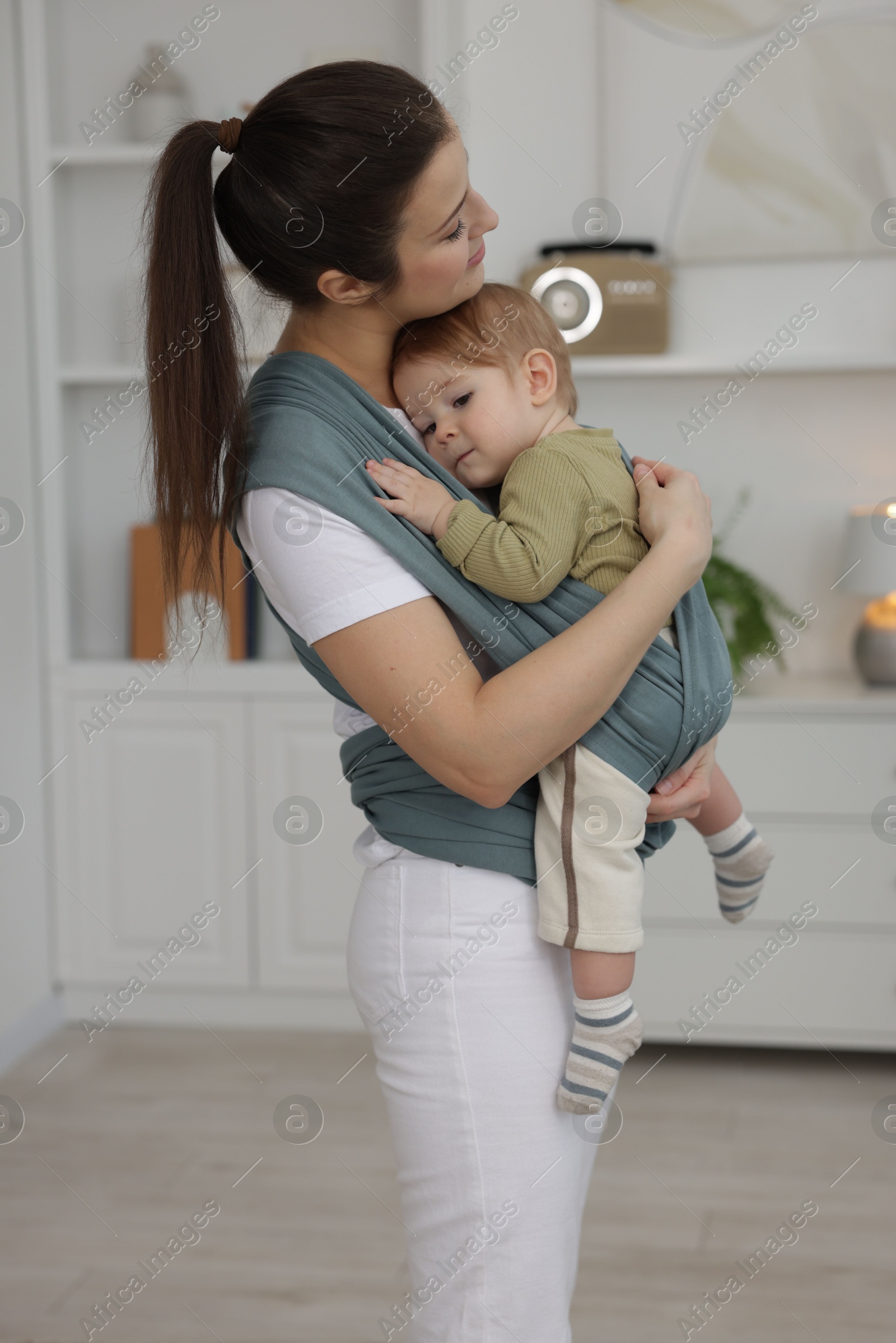 Photo of Mother holding her child in sling (baby carrier) at home