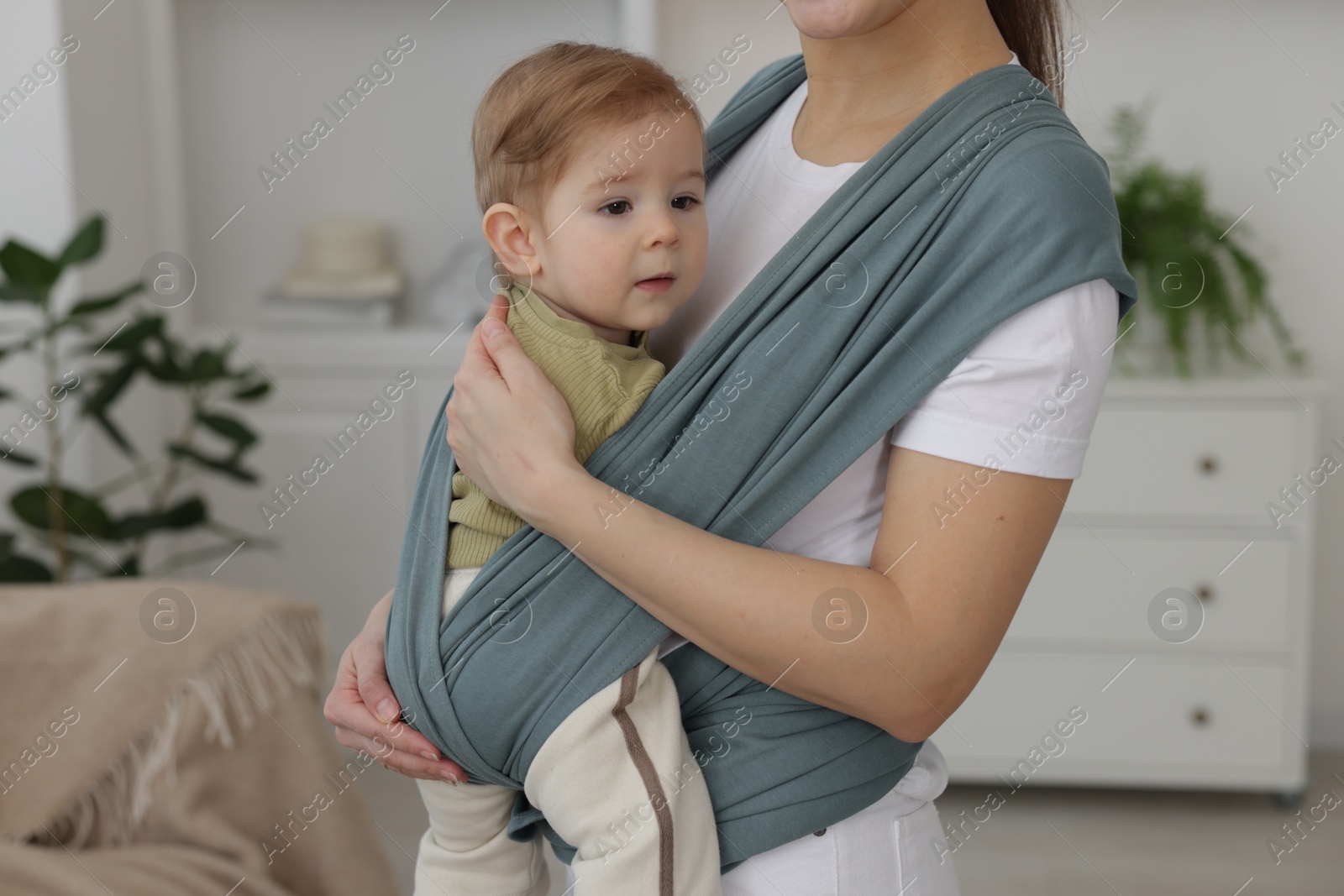 Photo of Mother holding her child in sling (baby carrier) at home, closeup