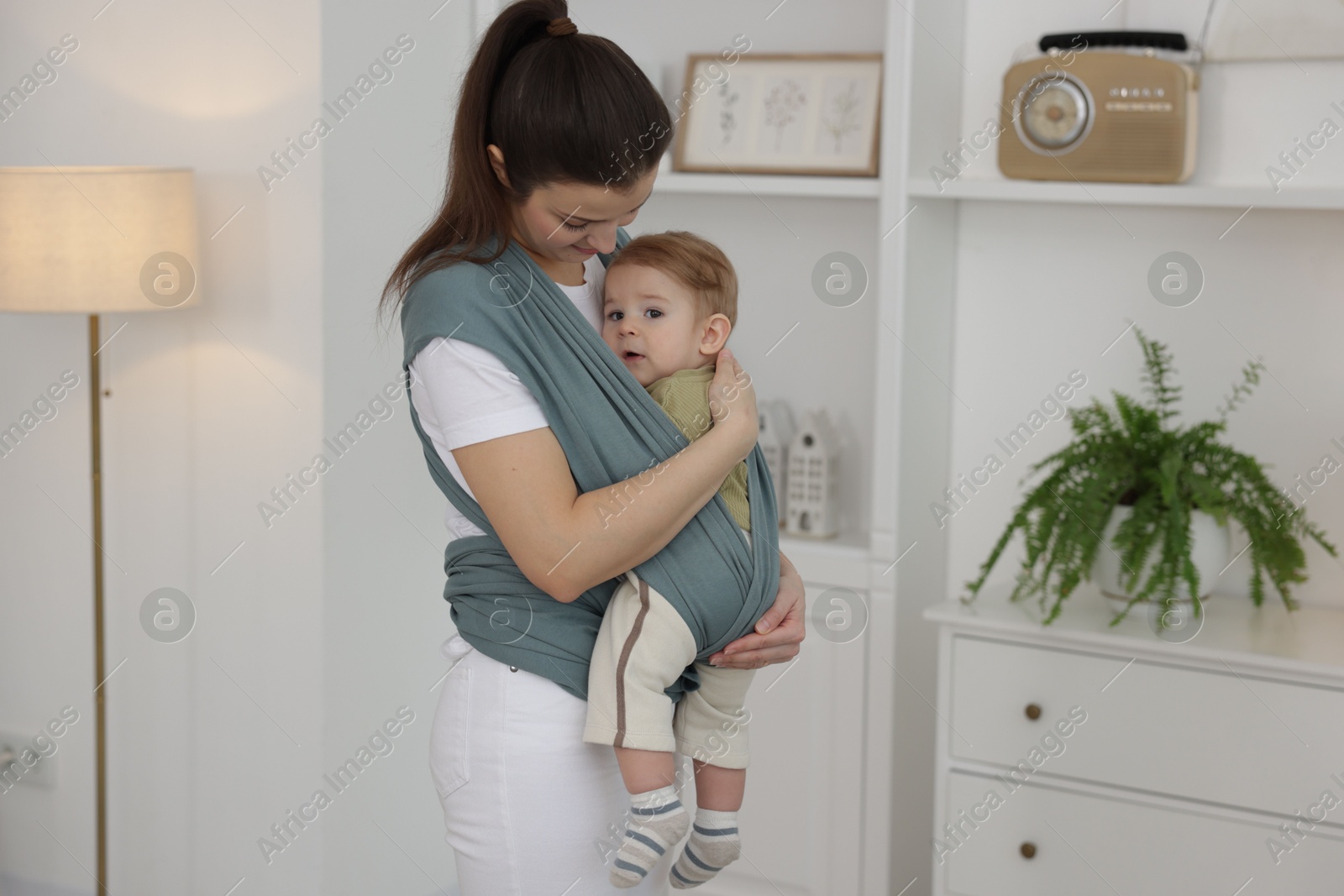 Photo of Mother holding her child in sling (baby carrier) at home