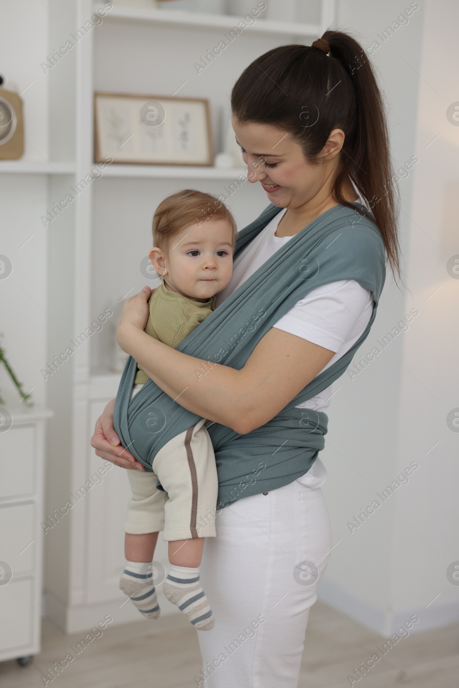 Photo of Mother holding her child in sling (baby carrier) at home