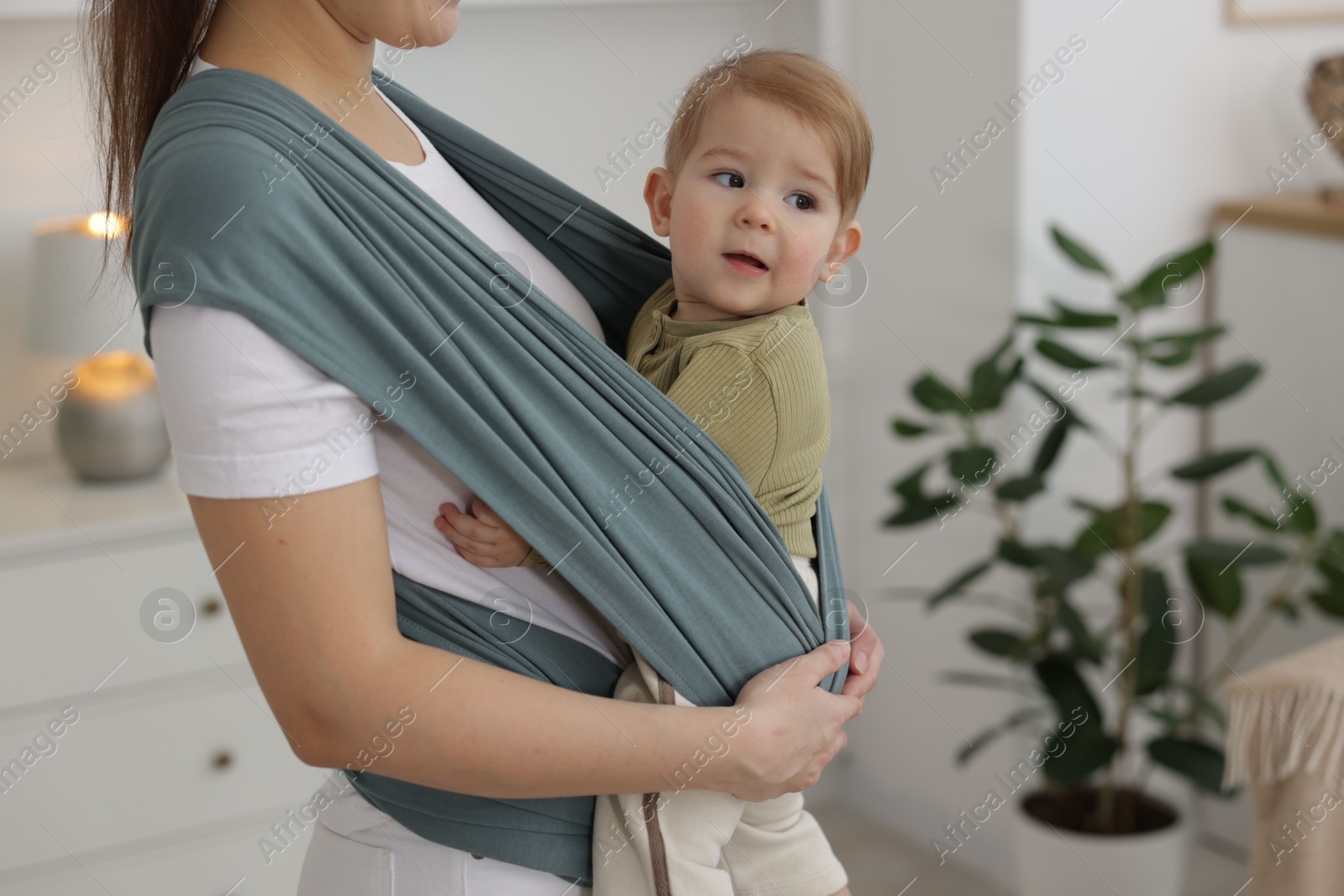 Photo of Mother holding her child in sling (baby carrier) at home, closeup. Space for text