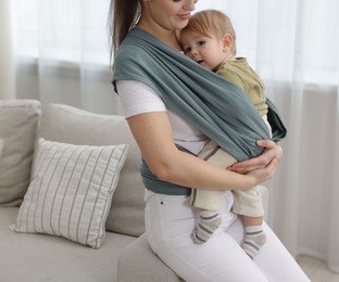 Mother holding her child in sling (baby carrier) at home, closeup