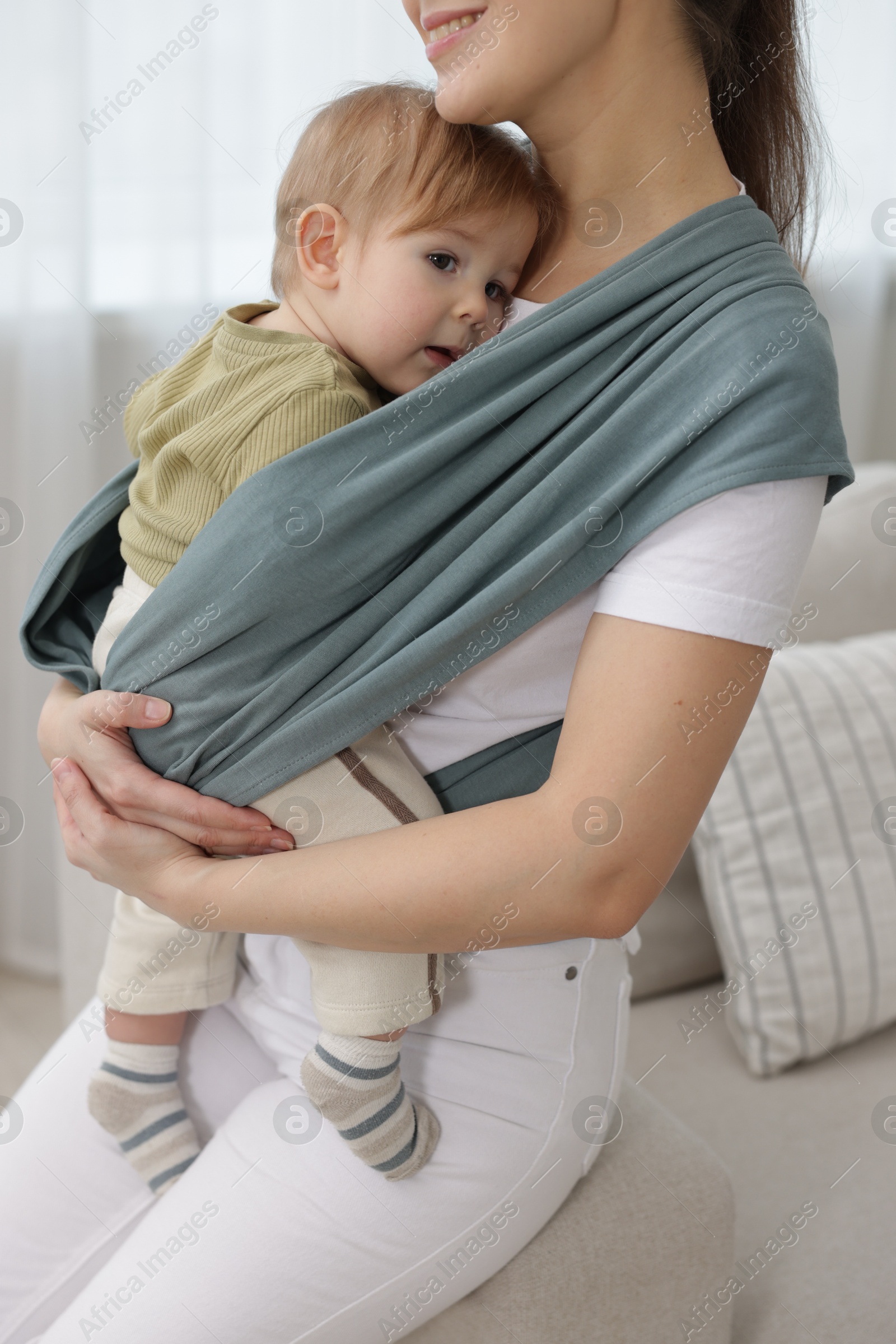 Photo of Mother holding her child in sling (baby carrier) at home, closeup