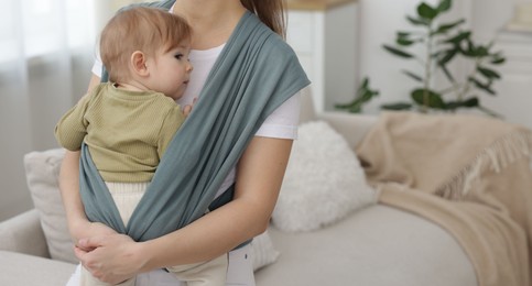 Photo of Mother holding her child in sling (baby carrier) at home, closeup. Space for text