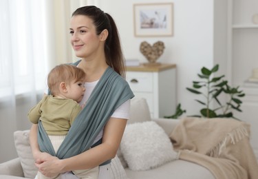 Mother holding her child in sling (baby carrier) at home, space for text