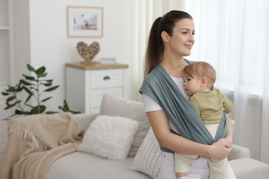 Mother holding her child in sling (baby carrier) at home, space for text