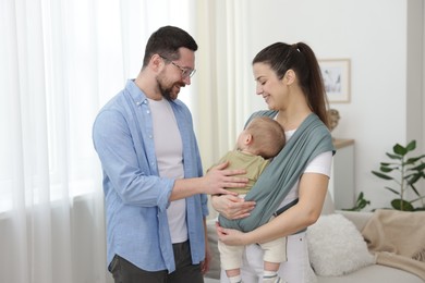 Photo of Portrait of happy family indoors. Mother holding her child in sling (baby carrier) at home