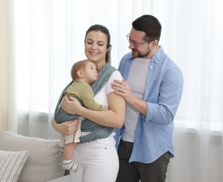 Portrait of happy family indoors. Mother holding her child in sling (baby carrier) at home