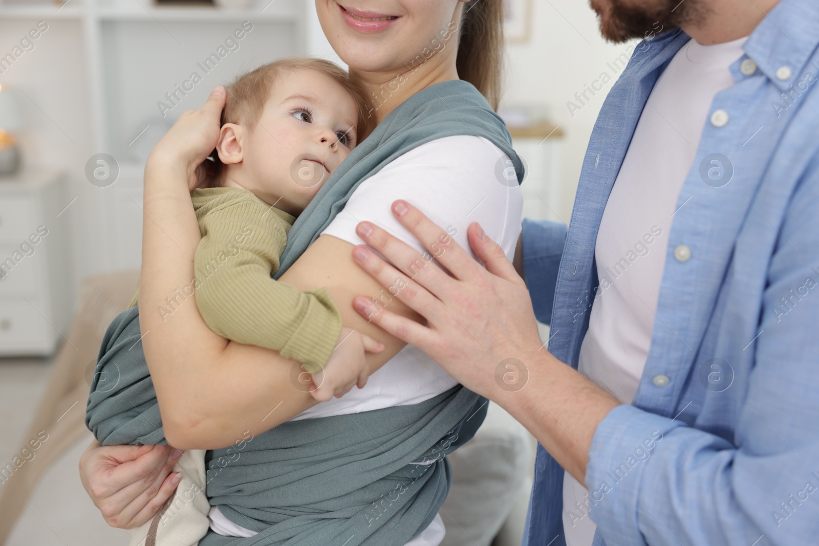 Photo of Parents with their baby indoors. Mother holding her child in sling at home, closeup