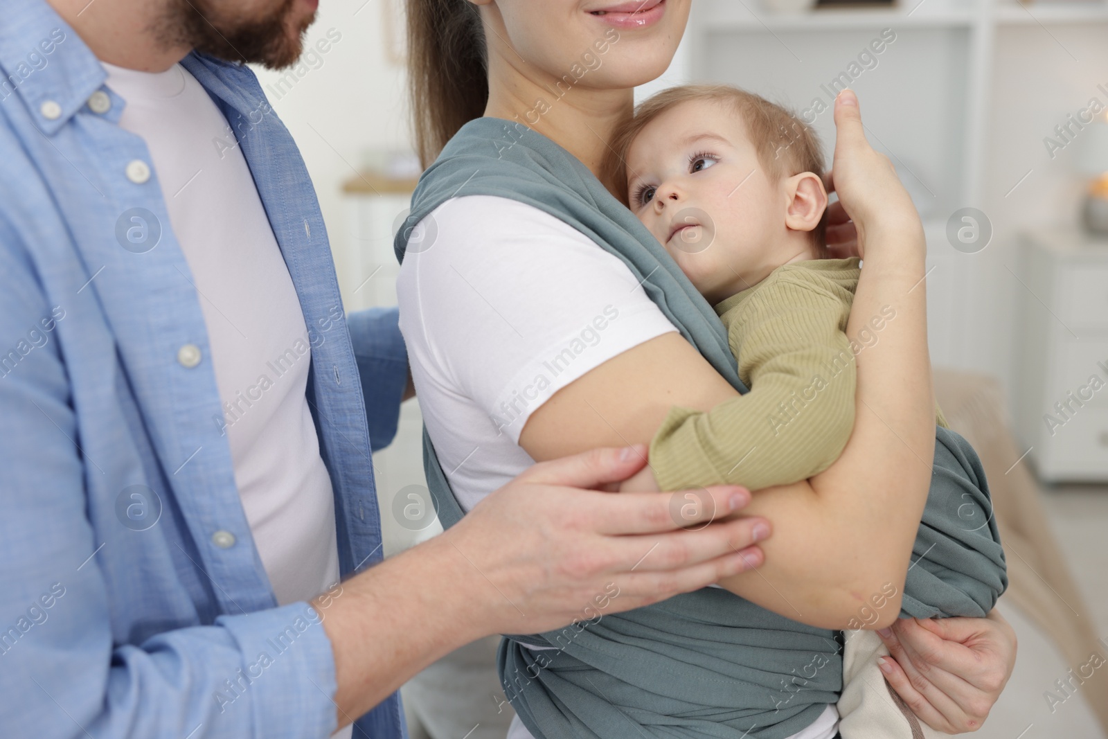 Photo of Parents with their baby indoors. Mother holding her child in sling at home, closeup