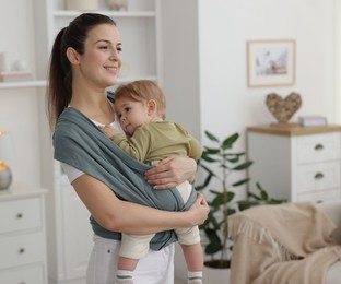 Mother holding her child in sling (baby carrier) at home, space for text