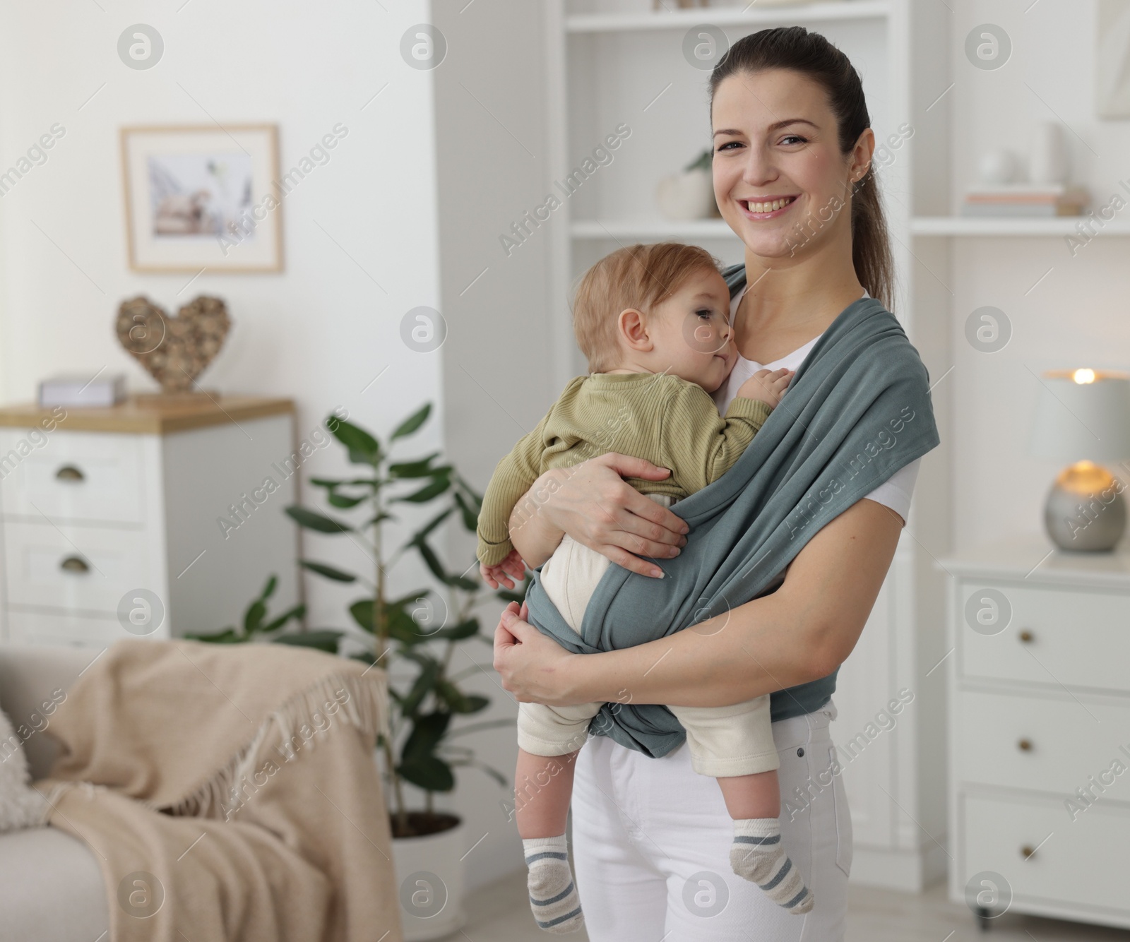 Photo of Mother holding her child in sling (baby carrier) at home, space for text