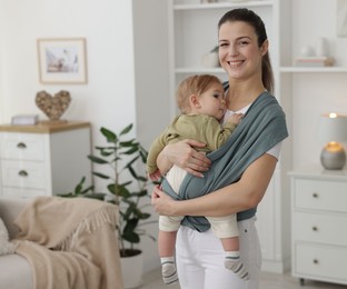 Mother holding her child in sling (baby carrier) at home, space for text