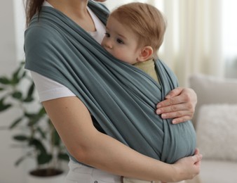 Photo of Mother holding her child in sling (baby carrier) at home, closeup