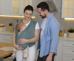 Portrait of happy family indoors. Mother holding her child in sling (baby carrier) at home