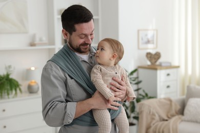 Photo of Father holding his child in sling (baby carrier) at home