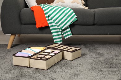 Photo of Organizers with folded clothes on gray rug indoors