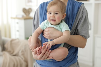 Mother holding her child in sling at home, closeup. Space for text