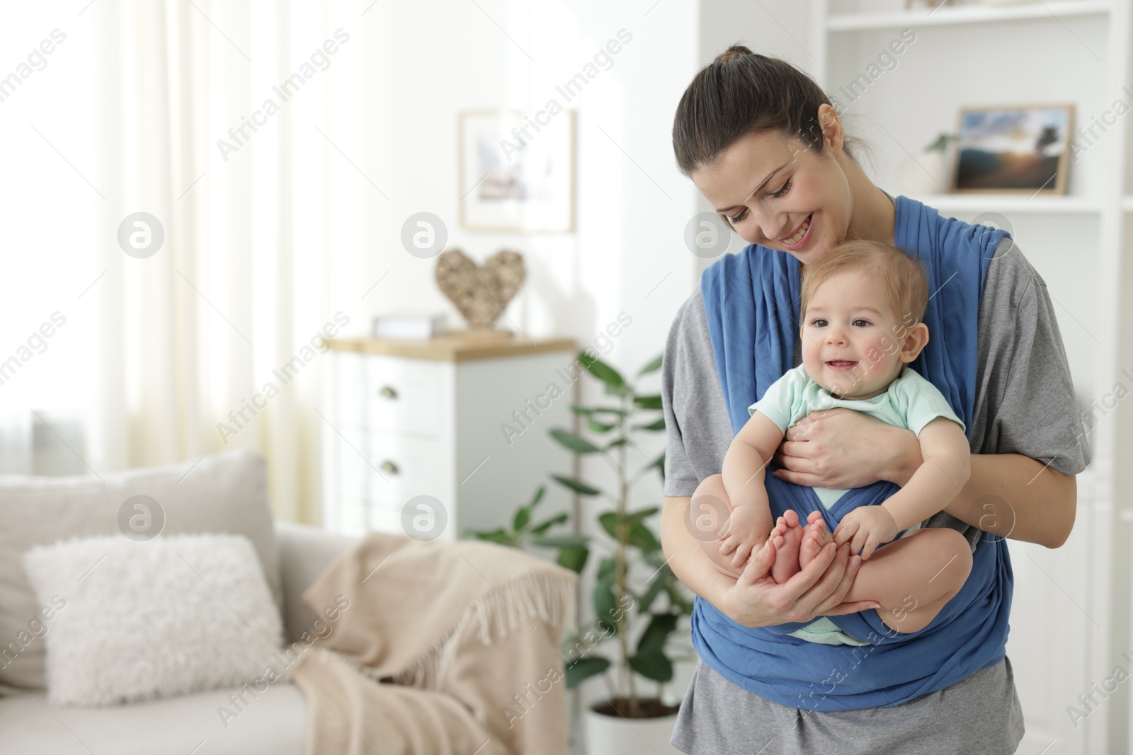 Photo of Mother holding her child in sling at home, space for text