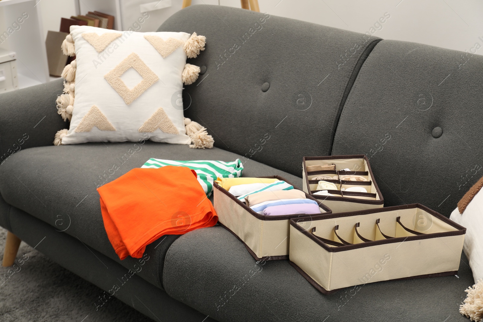 Photo of Organizers with folded clothes on gray sofa indoors