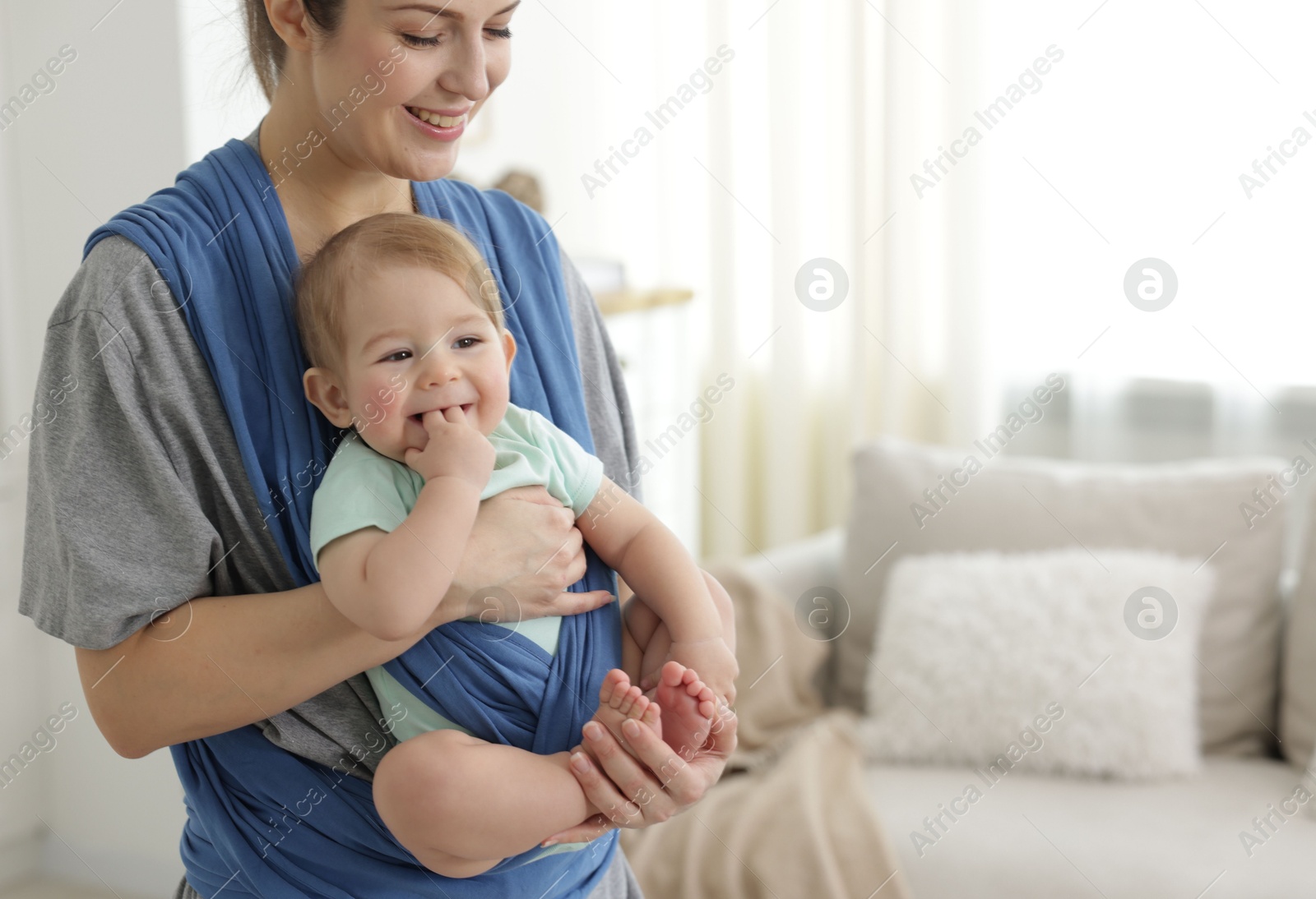 Photo of Mother holding her child in sling at home, space for text