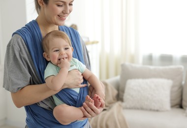 Mother holding her child in sling at home, space for text