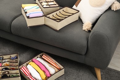 Photo of Organizers with folded clothes on gray sofa and rug indoors