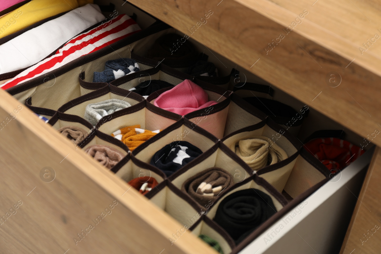 Photo of Organizers with different socks and folded clothes in drawer, closeup