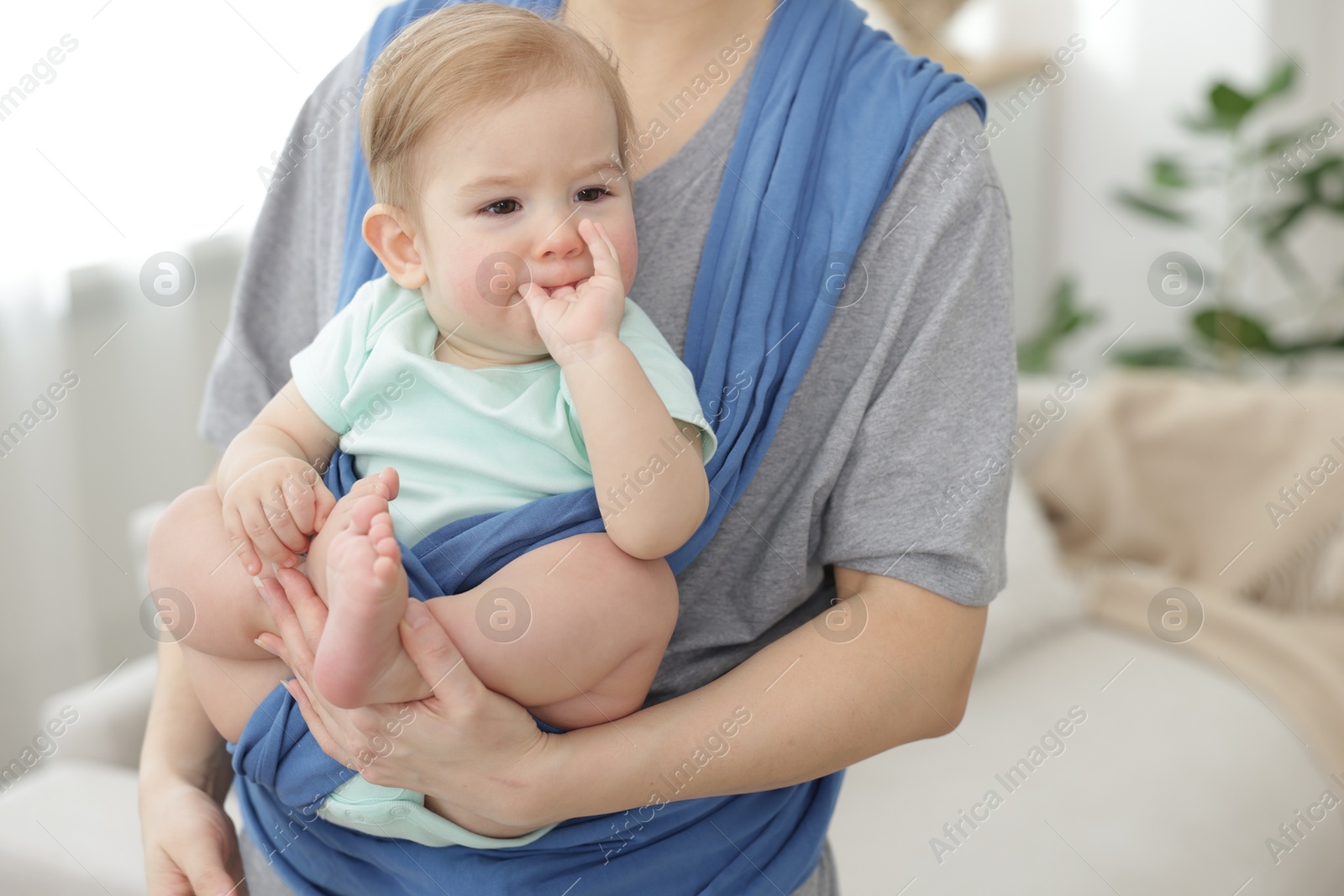 Photo of Mother holding her child in sling at home, closeup