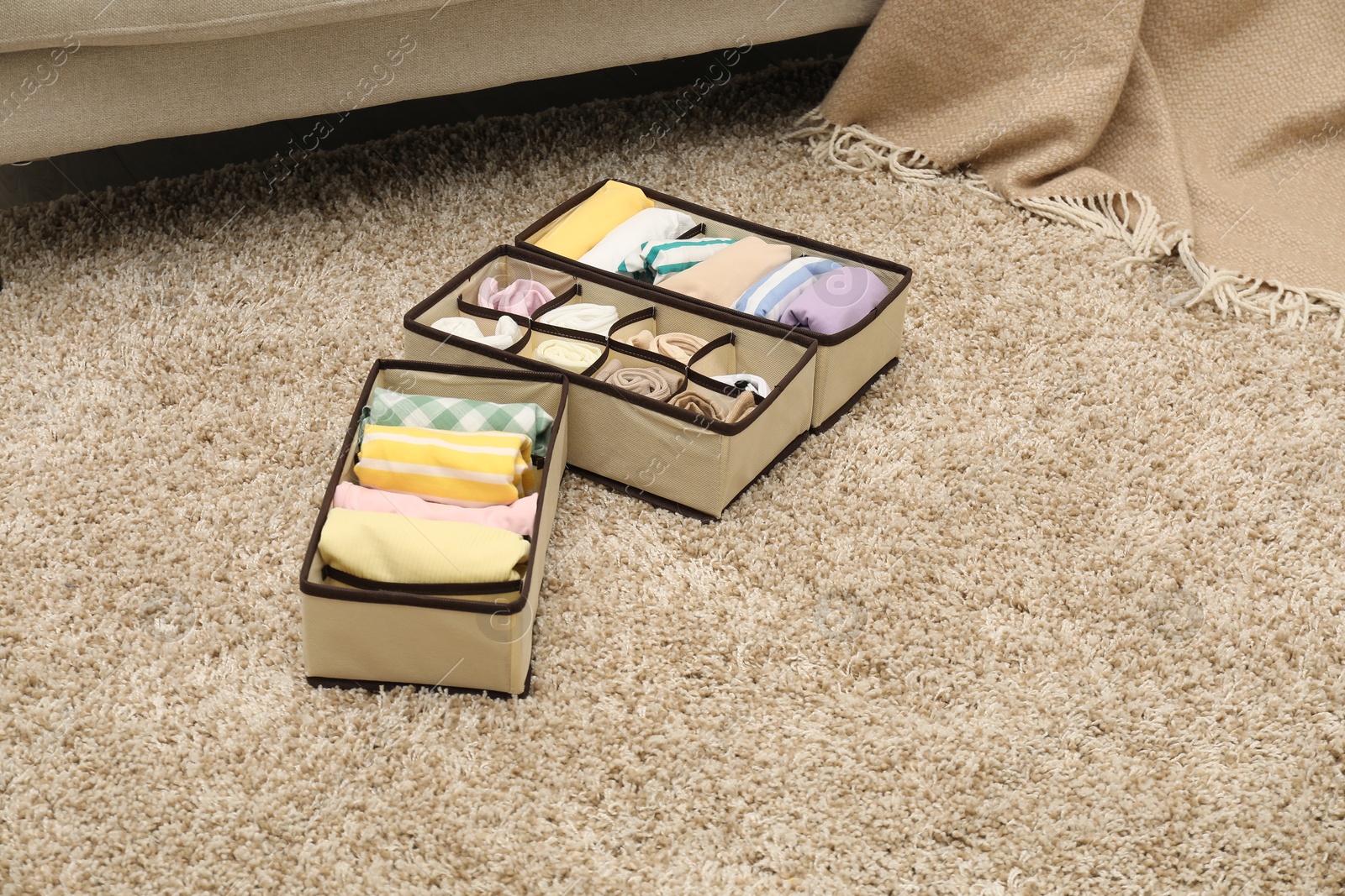 Photo of Organizers with folded clothes on rug indoors