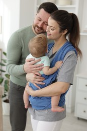 Portrait of happy family indoors. Mother holding her child in sling (baby carrier) at home