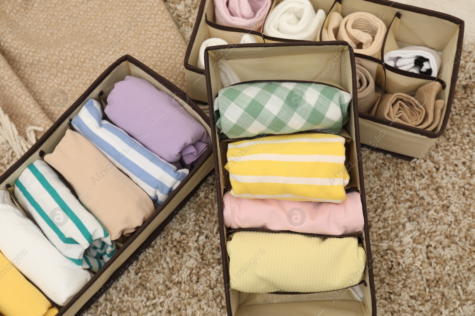 Photo of Organizers with folded clothes on rug indoors, top view